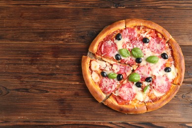 Photo of Tasty pizza with salami, cheese, basil and olives on wooden table, top view. Space for text