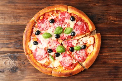 Photo of Tasty pizza with salami, cheese, basil and olives on wooden table, top view