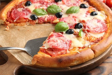 Photo of Tasty pizza with salami, cheese, basil and olives on wooden table, closeup