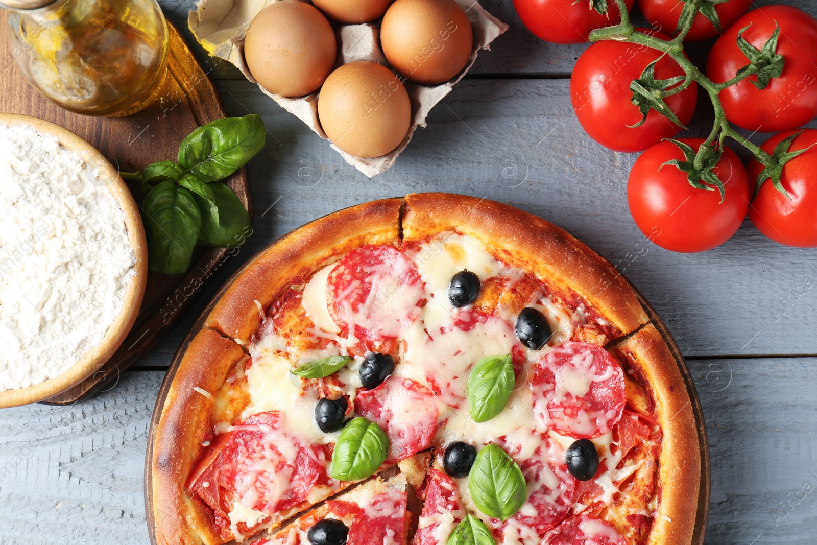Tasty pizza and ingredients on grey wooden table, flat lay Photo of Tasty pizza and ingredients on grey wooden table, flat lay