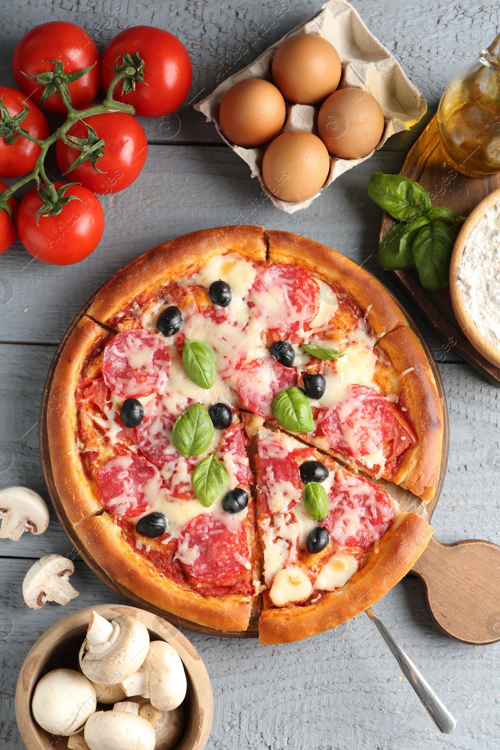 Tasty pizza and ingredients on grey wooden table, flat lay Photo of Tasty pizza and ingredients on grey wooden table, flat lay