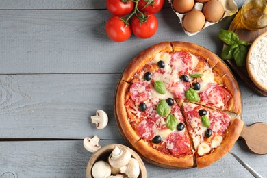 Photo of Tasty pizza and ingredients on grey wooden table, flat lay. Space for text
