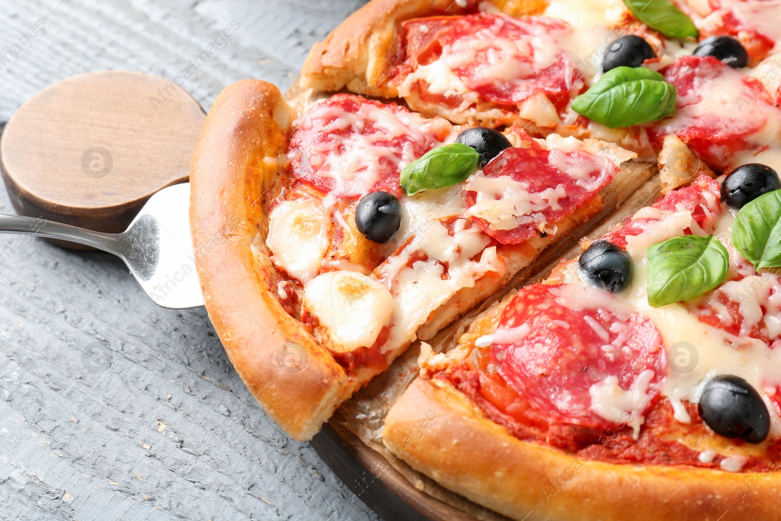 Tasty pizza with salami, cheese, basil and olives on grey wooden table, closeup Photo of Tasty pizza with salami, cheese, basil and olives on grey wooden table, closeup
