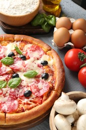 Photo of Tasty pizza and ingredients on grey wooden table, closeup