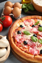 Photo of Tasty pizza and ingredients on grey wooden table, closeup
