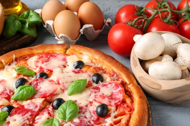 Photo of Tasty pizza and ingredients on grey wooden table, closeup