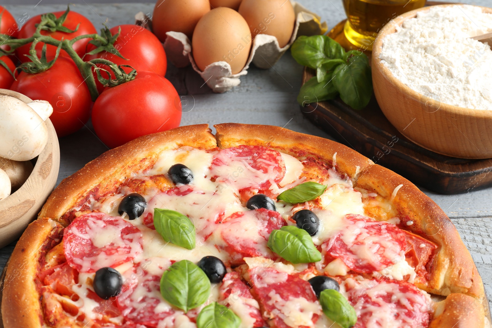 Tasty pizza and ingredients on grey wooden table, closeup Photo of Tasty pizza and ingredients on grey wooden table, closeup