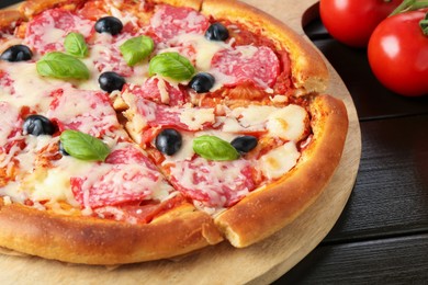 Photo of Tasty pizza with salami, cheese, basil and olives on black wooden table, closeup