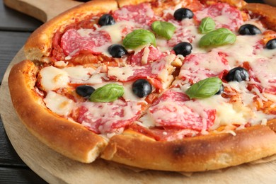 Photo of Tasty pizza with salami, cheese, basil and olives on table, closeup