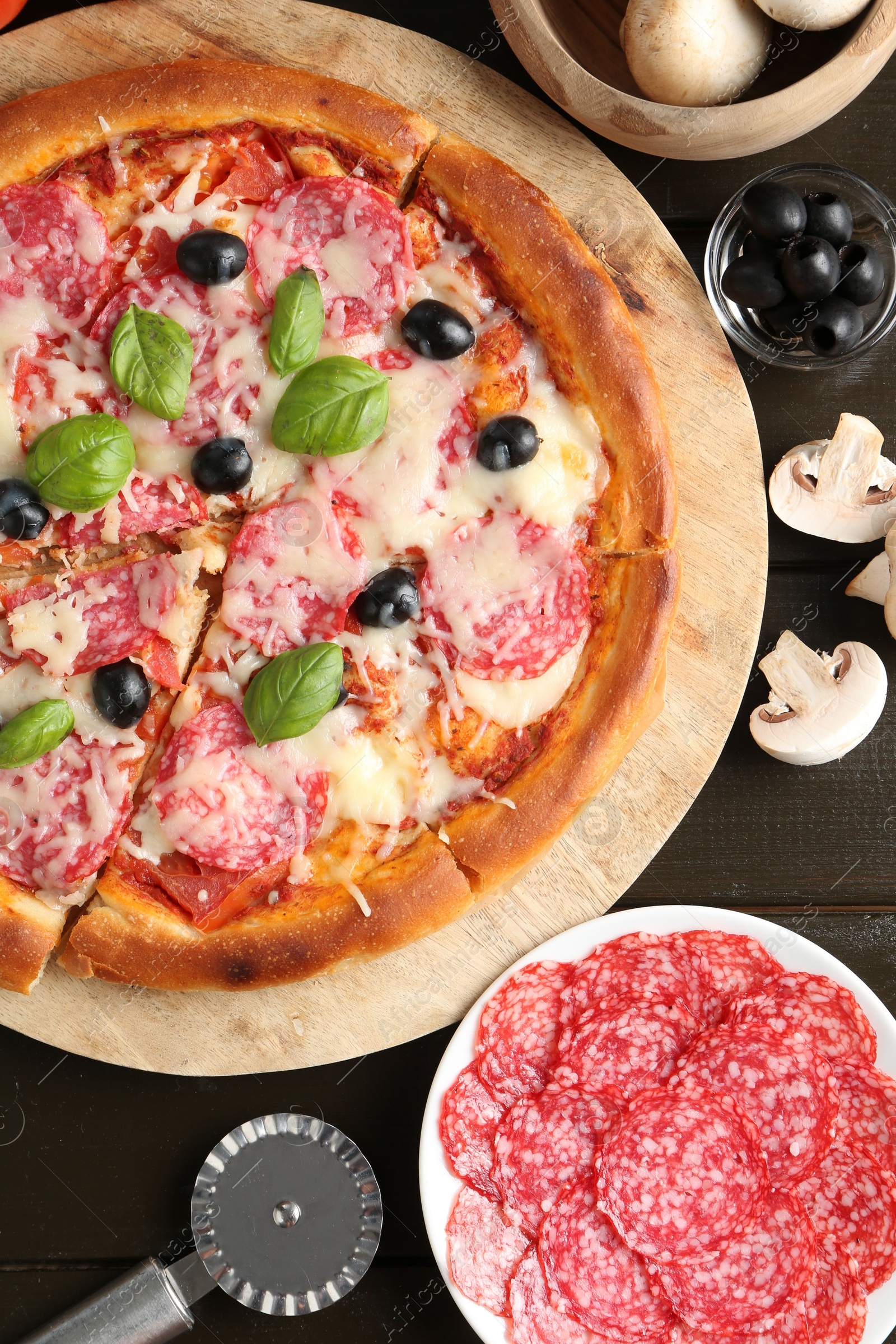 Tasty pizza, ingredients and cutter on black wooden table, flat lay Photo of Tasty pizza, ingredients and cutter on black wooden table, flat lay