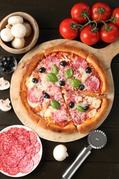 Photo of Tasty pizza, ingredients and cutter on black wooden table, flat lay