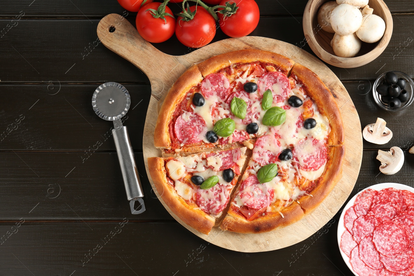Tasty pizza, ingredients and cutter on black wooden table, flat lay. Space for text Photo of Tasty pizza, ingredients and cutter on black wooden table, flat lay. Space for text