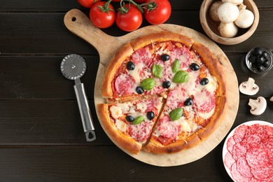 Photo of Tasty pizza, ingredients and cutter on black wooden table, flat lay. Space for text