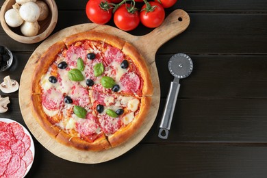 Photo of Tasty pizza, ingredients and cutter on black wooden table, flat lay. Space for text