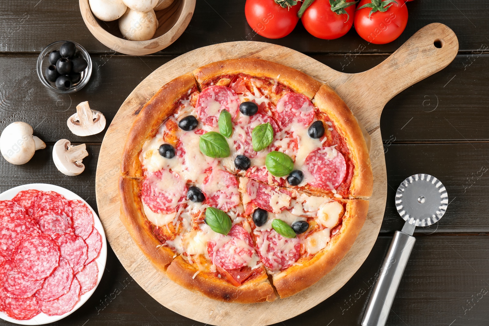 Tasty pizza, ingredients and cutter on black wooden table, flat lay Photo of Tasty pizza, ingredients and cutter on black wooden table, flat lay
