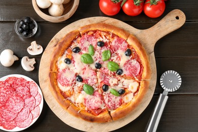 Photo of Tasty pizza, ingredients and cutter on black wooden table, flat lay