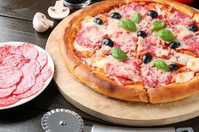 Photo of Tasty pizza, ingredients and cutter on black wooden table, closeup