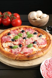Photo of Tasty pizza and ingredients on black wooden table, closeup