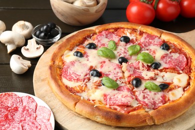 Photo of Tasty pizza and ingredients on black wooden table, closeup