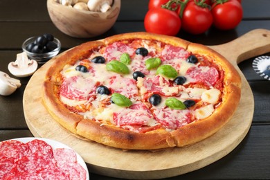 Photo of Tasty pizza and ingredients on black wooden table, closeup