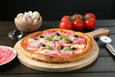 Photo of Tasty pizza, ingredients and cutter on black wooden table, closeup
