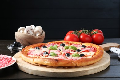 Photo of Tasty pizza, ingredients and cutter on black wooden table, closeup