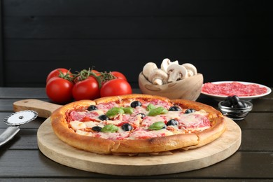 Photo of Tasty pizza, ingredients and cutter on black wooden table, closeup