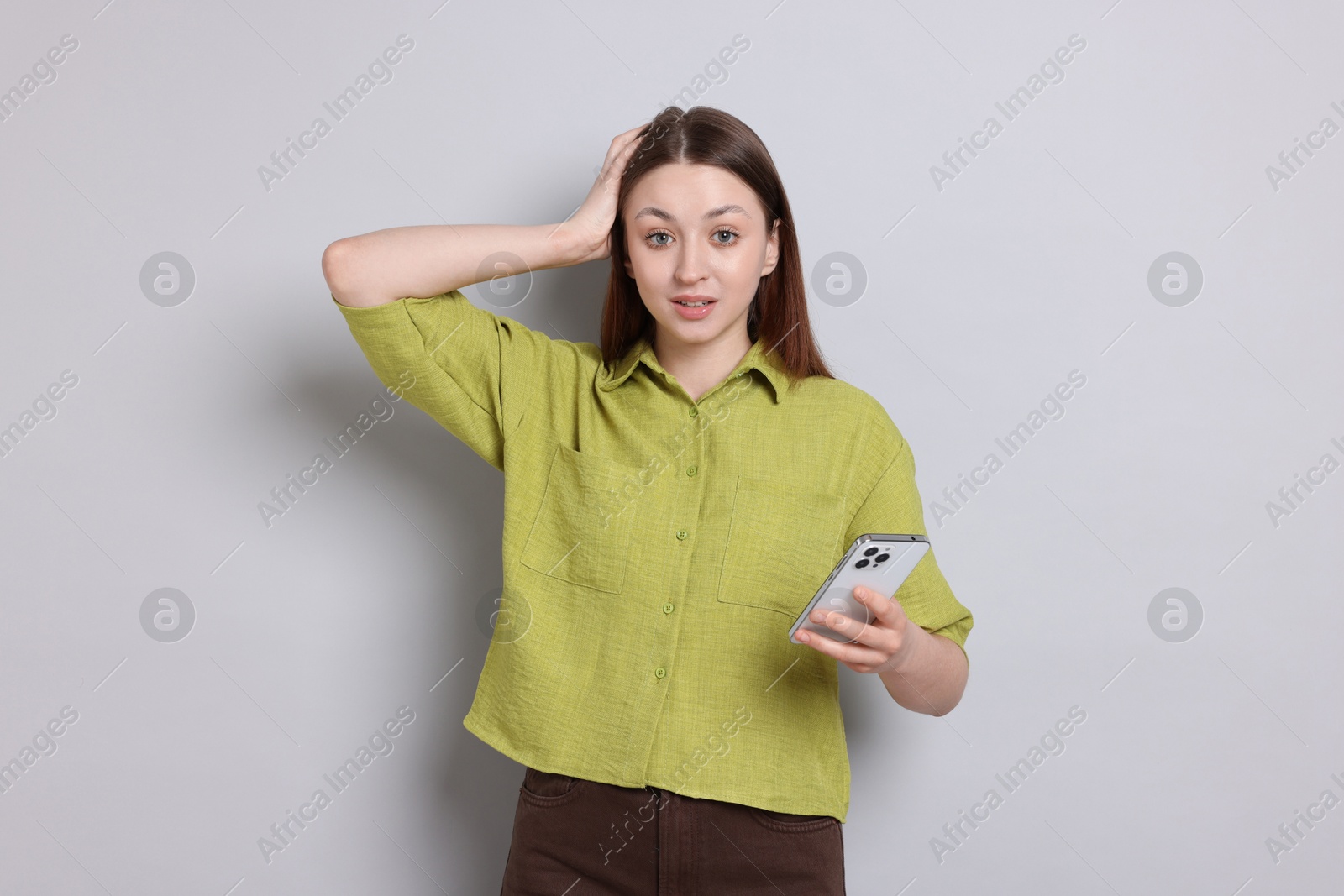 Teenage girl with smartphone on light grey background Photo of Teenage girl with smartphone on light grey background