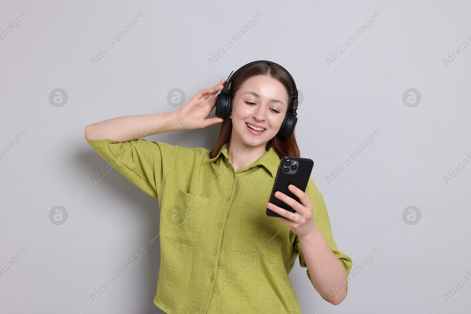 Photo of Happy teenage girl in headphones using smartphone on light grey background