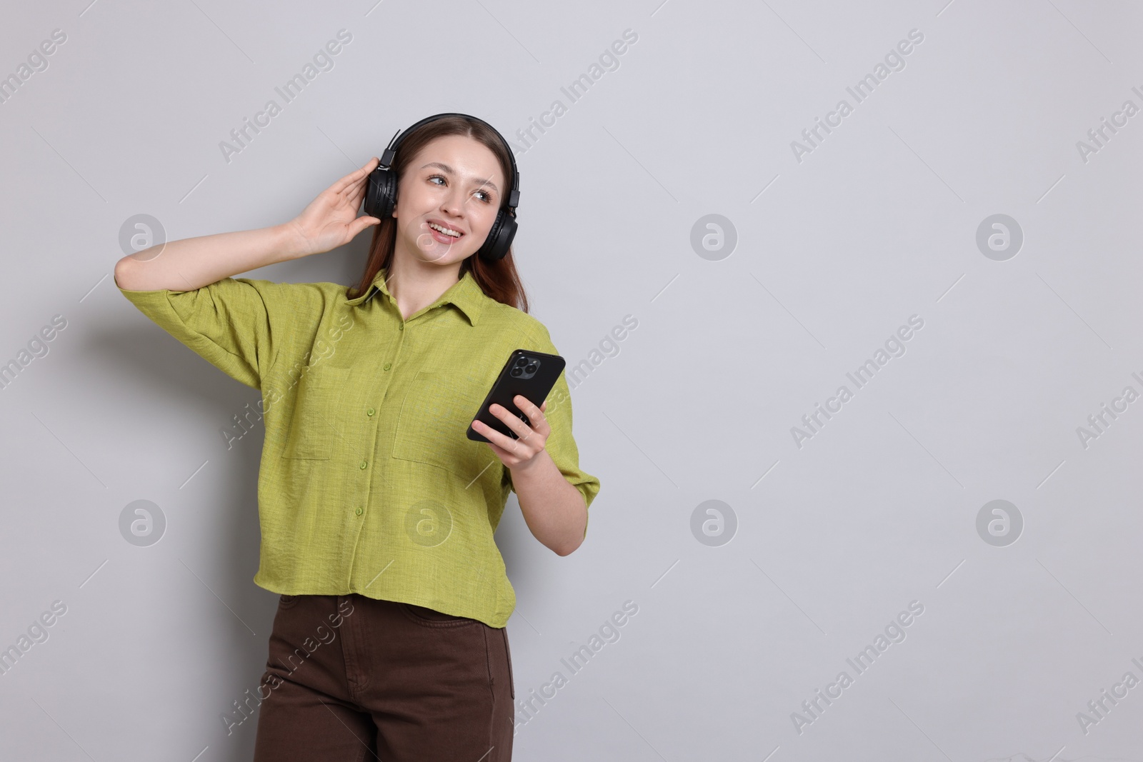 Happy teenage girl in headphones using smartphone on light grey background, space for text Photo of Happy teenage girl in headphones using smartphone on light grey background, space for text