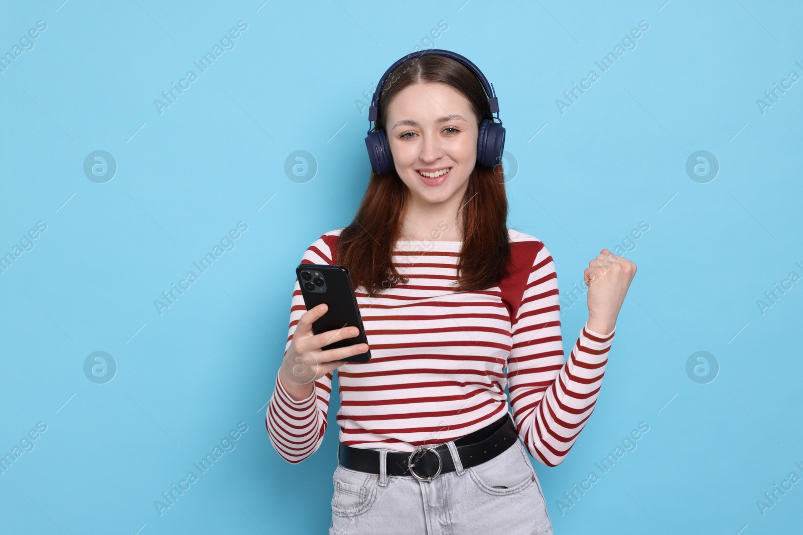 Teenage girl in headphones using smartphone on light blue background Photo of Teenage girl in headphones using smartphone on light blue background