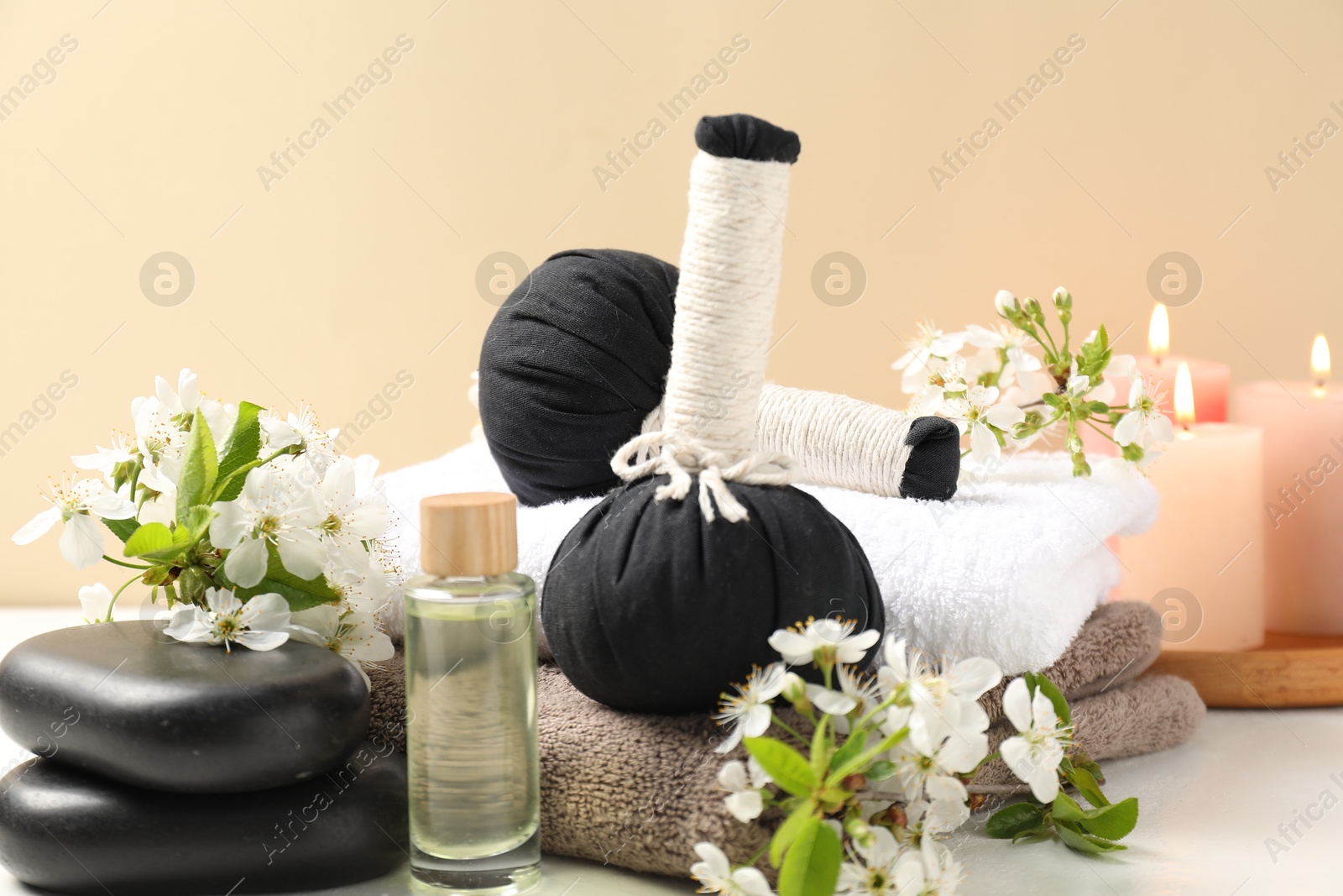 Spa composition with herbal bags, beautiful flowers and burning candles on white table against beige background, closeup Photo of Spa composition with herbal bags, beautiful flowers and burning candles on white table against beige background, closeup