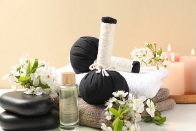 Photo of Spa composition with herbal bags, beautiful flowers and burning candles on white table against beige background, closeup