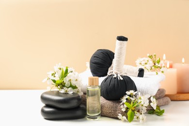 Photo of Spa composition with herbal bags, beautiful flowers and burning candles on white table against beige background