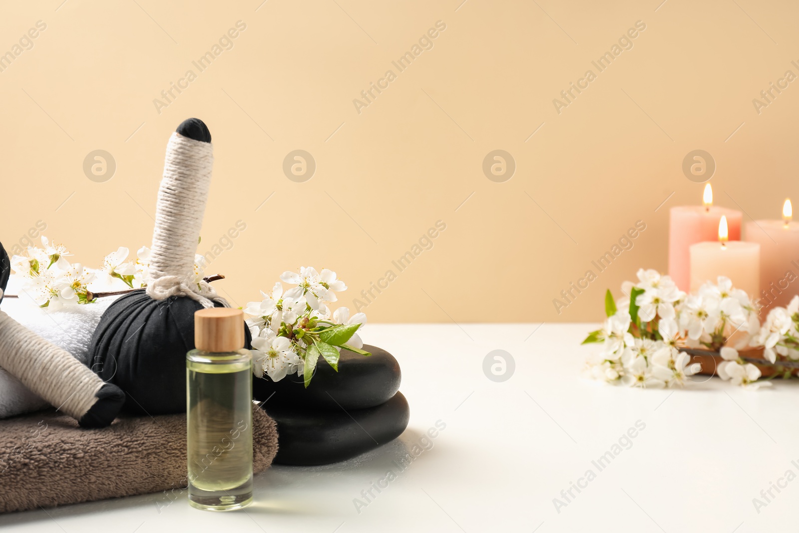 Spa composition with herbal bags, beautiful flowers and burning candles on white table against beige background Photo of Spa composition with herbal bags, beautiful flowers and burning candles on white table against beige background