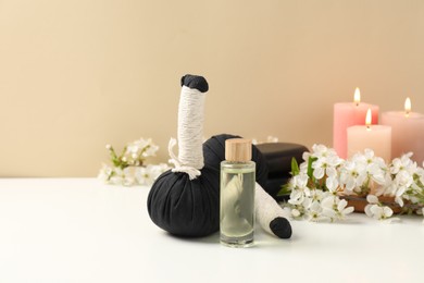 Photo of Spa composition with herbal bags, beautiful flowers and burning candles on white table against beige background