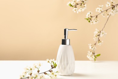 Photo of Bottle of cosmetic product and twigs with beautiful flowers on white table against beige background