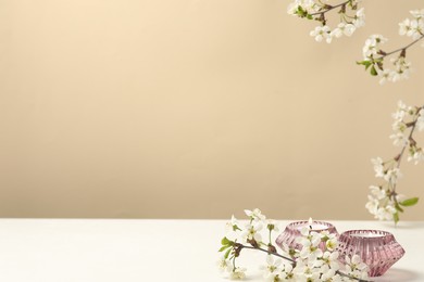 Photo of Burning candles and twigs with beautiful flowers on white table against beige background. Space for design