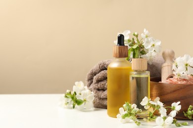 Photo of Spa composition with cosmetic products and beautiful flowers on white table against beige background, space for text