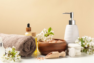 Photo of Spa composition with cosmetic products and beautiful flowers on white table against beige background