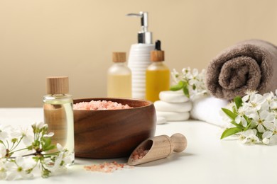 Photo of Spa composition with cosmetic products and beautiful flowers on white table against beige background, selective focus