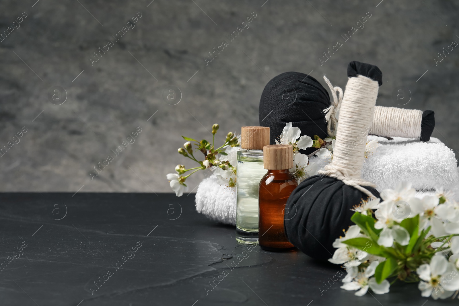 Spa composition with cosmetic products and beautiful flowers on black textured table against gray background, space for text Photo of Spa composition with cosmetic products and beautiful flowers on black textured table against gray background, space for text