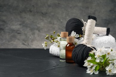 Photo of Spa composition with cosmetic products and beautiful flowers on black textured table against gray background, space for text