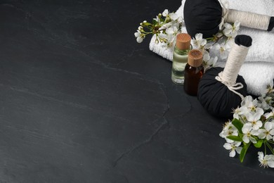Photo of Spa composition with cosmetic products and beautiful flowers on black textured table, space for text