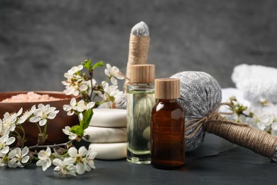 Photo of Spa composition with cosmetic products and beautiful flowers on black textured table, closeup