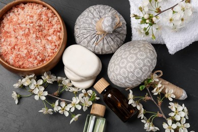 Photo of Spa composition with cosmetic products and beautiful flowers on black textured table, flat lay