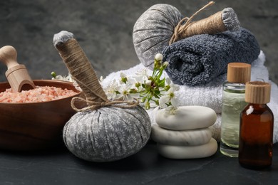 Photo of Spa composition with cosmetic products and beautiful flowers on black textured table, closeup