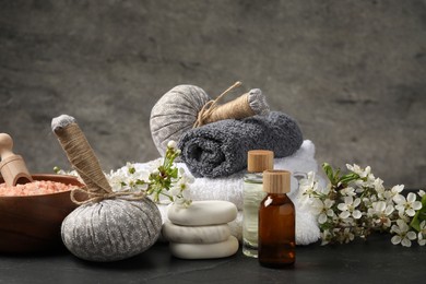 Photo of Spa composition with cosmetic products and beautiful flowers on black textured table against gray background