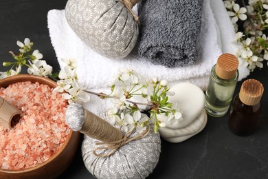 Photo of Spa composition with cosmetic products and beautiful flowers on black textured table, closeup