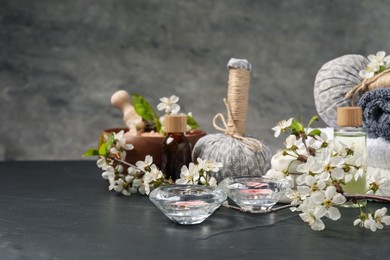Photo of Spa composition with cosmetic products, burning candles and beautiful flowers on black textured table against gray background